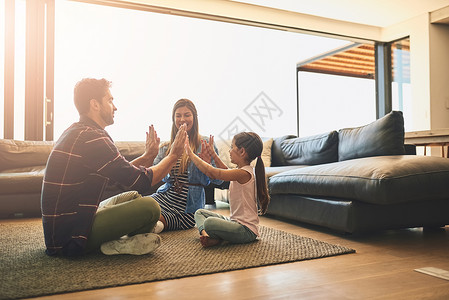 玩得开心时 家庭时间会更好 一个三人的快乐家庭在家里一起打拍掌游戏的照片 (笑声)背景图片