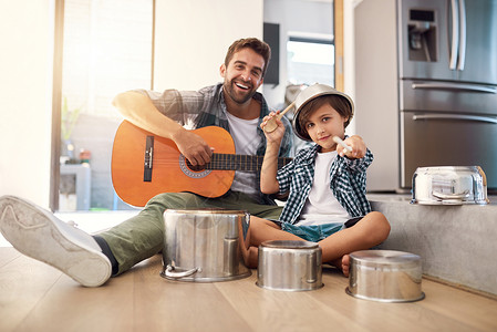 他吉他的父亲一个快乐父亲的肖像 陪着他年轻的儿子坐在吉他上 而他却在一套锅里鼓起鼓声来背景