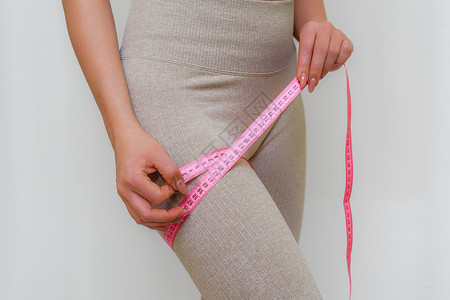 苗条女人在家里用卷尺测量她的腿的剪影 特写 一位面目全非的欧洲女性在室内检查减肥饮食或抽脂的结果 健康的生活方式动机身体数字重量背景图片
