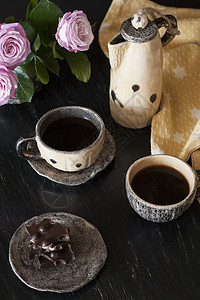 两杯黑咖啡 黑色巧克力 一个黄茶壶和一个花瓶 底底有粉红玫瑰黄色坚果玫瑰咖啡机休息餐巾杯子早餐背景图片