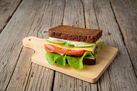 深色木质背景中的三明治 配黑麦面包 火腿 奶酪 西红柿 黄瓜 生菜背景图片