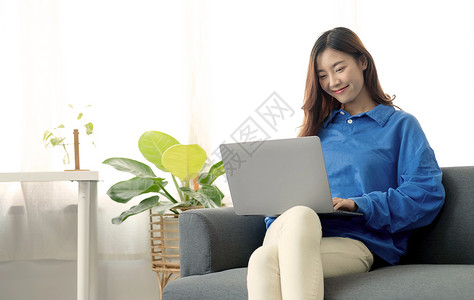 索拉沙年轻商业自由职业亚洲女性在社会媒体检查笔记本电脑上工作 而躺在沙发上时却在家里的客厅放松知识购物者长椅公寓家庭作业网上购物闲暇拉背景