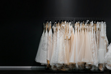 左侧肛提肌腱弓由真丝雪纺 薄纱和蕾丝制成的婚纱 美丽的白色奶油色新娘礼服挂在婚礼沙龙的衣架上 广告文字左侧空白的照片背景