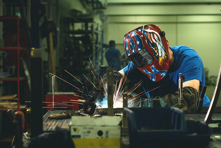 在工厂内工作的专业重工业焊工 戴着头盔并开始焊接 选择性焦点面具机器技术工程师职业火花商业作坊力量焊机背景图片