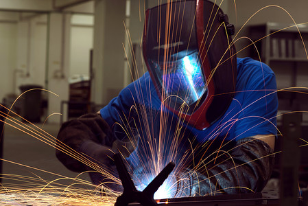在工厂内工作的专业重工业焊工 戴着头盔并开始焊接 选择性焦点火花男人职业机器职场维修闪光商业车间手套背景图片