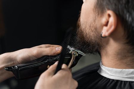 在理发店刮胡子 长着脚镣的理发师修剪英俊胡子的男人主义头发顾客胡须商业绅士男性剃刀潮人黑色背景图片