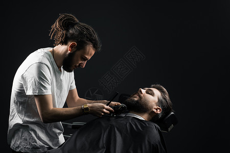 在理发店刮胡子 长着脚镣的理发师修剪英俊胡子的男人大男子男性胡须潮人剃须店铺客户理发顾客黑色背景图片