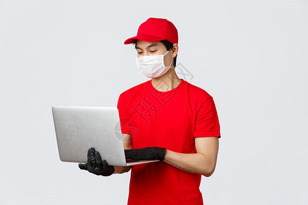 帅气的亚洲送货员 戴着医用口罩和手套 穿红帽制服 在网页上回答客户问题 使用笔记本电脑在快递服务中提供客户支持 搜索您的包裹载体背景图片