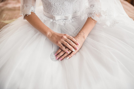 美皮肤新娘的女手 躺在白色婚纱上的白礼服上美甲蕾丝套装婚礼沙龙女士裙子乳罩证人玫瑰背景