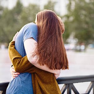 女孩有长长深暗的听力 在桥上拥抱红发男孩 日落时爱青少年背景图片