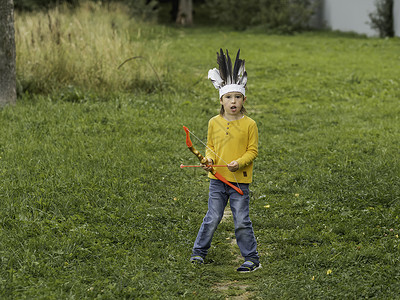 小男孩正在球场上打美洲印第安人 孩子有手工制作的羽毛头饰和带箭的蝴蝶结 古装角色扮演 户外休闲活动 金秋时节童年日光场地闲暇游戏背景图片