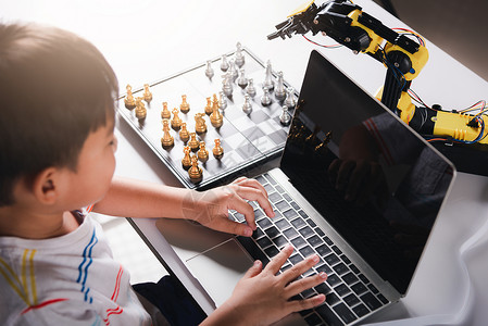 编程游戏亚洲小男孩编程代码 机器人机器臂在笔记本电脑上 用来玩象棋孩子学习教育技术学校实验幼儿园程序员机械电子产品背景