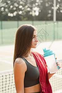 健身运动模式在经过训练后正在休息 饮用水来自瓶子 体育生活方式 网球场上美丽的女孩的姿势法庭减肥公园健身房闲暇乐趣运动装女性女士背景图片