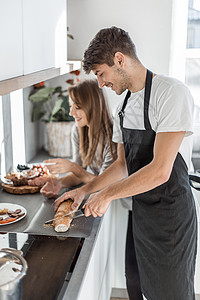 年轻情侣为早餐做三明治很快乐男性男人烹饪食物闲暇餐具夫妻房子用具面包背景图片