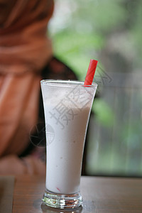 在咖啡馆喝香蕉奶昔的年轻妇女奶制品香蕉奶油眼镜白色女性液体牛奶饮料背景图片