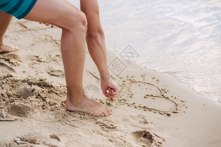 沙滩写字年轻人在沙滩上的沙子上写字 穿绿色短裤的男人 美丽干净的沙子背景