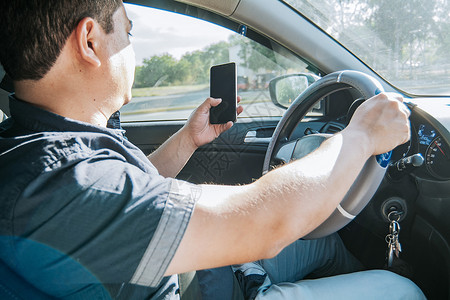 拿着手机的人 另一只手拿着方向盘 开车时用手机的人 不负责任驾驶的概念 开车时用手机分心的司机背景图片
