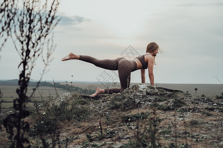 山顶瑜伽在山顶进行伸展运动的体育女运动员 在日落日落开展青年妇女练习瑜伽外门女孩姿势女性成人爬坡自由日出身体冥想岩石背景