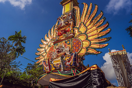 印度尼西亚巴厘岛乌布德市中央街道上 传统恶魔的拜林树雕塑和鲜花组成的巴德火化塔 为即将到来的火化仪式做准备塑像水牛男人佛教徒雕像背景图片