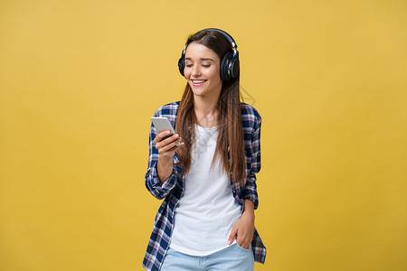 在耳机中听音乐和歌唱黄色背景的美丽的年轻女青春女子工具播放表演收音机享受舞蹈女性电话旋律女孩背景图片