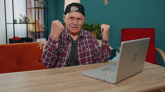 带着笔记本电脑的曾祖父大喜若狂 在网上彩票好消息中庆祝成功赢钱背景图片