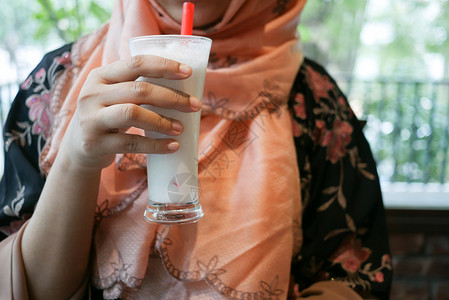 在咖啡馆喝香蕉奶昔的年轻妇女液体奶油牛奶眼镜白色奶制品女性香蕉饮料背景图片