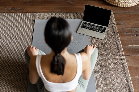 正念和冥想的概念 亚洲年轻女性在家中冥想的后视图 她们在笔记本电脑上完成在线课程 坐在客厅的地垫上女孩成人技术互联网瑜伽运动装重背景