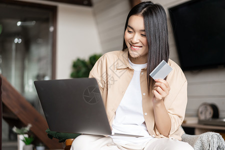 亚洲女孩用信用卡 使用笔记本电脑 在网站上购买网上购入命令支付福利乐趣房子女性互联网家具学生房间背景图片