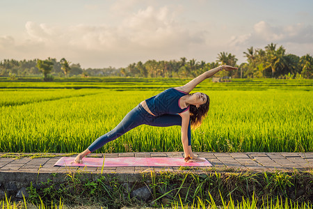 年轻女性在巴厘健康务虚会当天早上在稻田户外做瑜伽姿势运动专注女士丛林身体成人平衡女孩训练背景