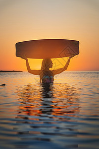 齐腰深的水穿着潜水服的迷人年轻女子站在齐腰深的海水中 头上拿着风筝冲浪板 描绘了古埃及图案背景