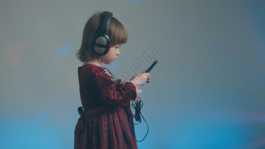 穿着大耳机和古代礼服的小女孩 在电话里听音乐婴儿衣服连衣裙爱好玩家家庭宝宝乐器蕾丝孩子们背景图片