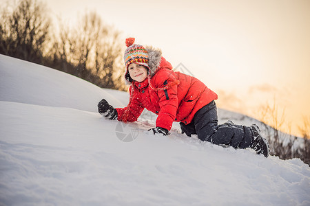 滚雪球的男孩穿着红色时装的男孩在户外玩耍 在寒冷的日子里 在冬天与孩子们一起积极休闲 男孩玩第一场雪 快乐的小孩在雪地里玩耍 冬天天气很好场背景