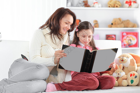 沙发上的书有魅力的母亲和女儿在沙发上读一本书 照片附影空间背景