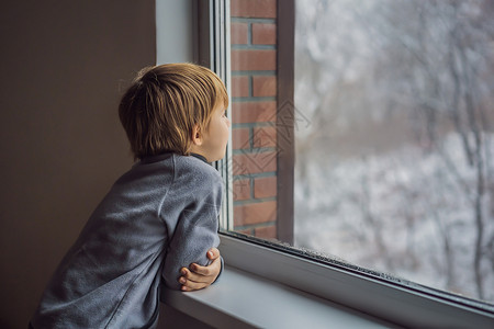 圣诞节那天或早上 快乐可爱的男孩坐在窗边 看着外面的雪 微笑的孩子着迷于降雪和大雪花毛衣金发乐趣假期眼睛小学生童年游客男生运输背景图片