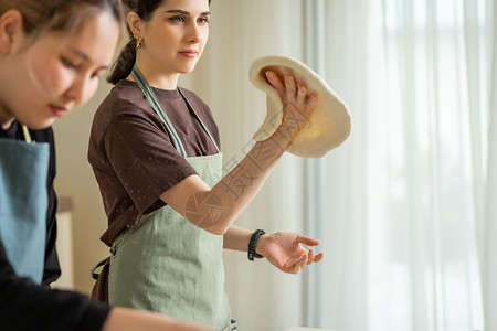 两个年轻的女厨师 在厨房做比萨饼 一个扭曲她手上的卷钱背景图片