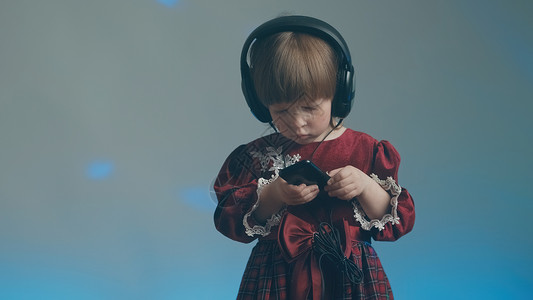 穿着大耳机和古代礼服的小女孩 在电话里听音乐复古衣服乐器蓝色婴儿玩家裙子宝宝长袍工具背景图片