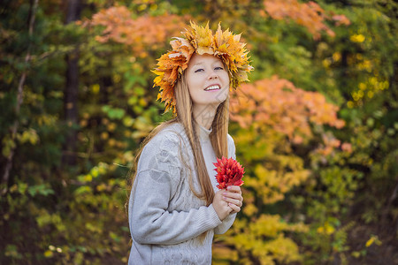 枫叶花圈户外生活方式特写迷人的金发年轻女子的画像 她戴着秋叶花环 微笑着 走在秋天的公园里 穿着时尚的针织套头衫 枫叶花环背景