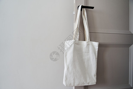 手提袋模板白色生态友好袋挂在门把手上 罐装袋女性顾客手工材料女手亚麻帆布包木材市场样机背景