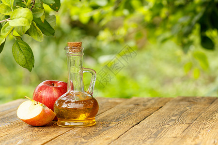 苹果酒玻璃瓶中的苹果醋和木板上新鲜的红苹果水果食物液体果汁乡村玻璃绿色红色瓶子桌子背景