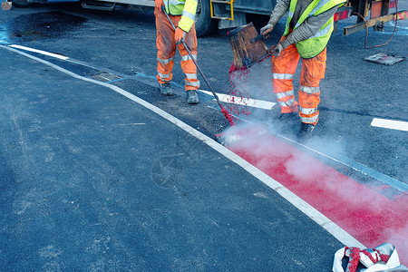 公路网在新建设公路上涂贴热红色道路标识油漆的公路工人修路活动交通施工投资建造路面标记工地安全背景