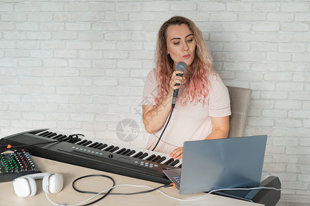 钢琴开课了一位女士在家中使用笔记本电脑录制声乐课程 并在键盘上伴奏 老师对着话筒唱了一首歌 并弹奏了电子钢琴 博主正在录制视频歌曲博客电子背景