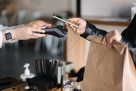 年轻女子在咖啡馆使用 NFC 技术通过智能手机支付账单 女性顾客使用非接触式技术付款 咖啡店移动支付的特写手信用卡高清图片素材