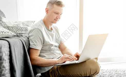 英俊的年轻人在笔记本电脑上工作自由职业者男性成人技术沙发客厅枕头办公工作者男人快乐的高清图片素材