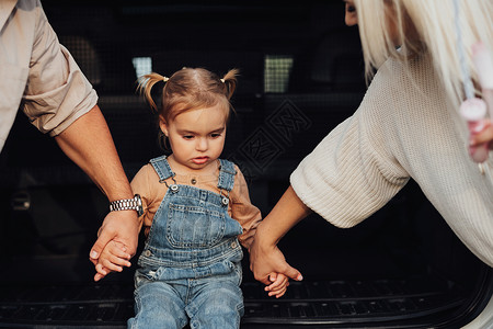 坐在汽车露天车轮的小女孩 她的父母亲亲亲手扶住她 帮助挺身而出背景图片