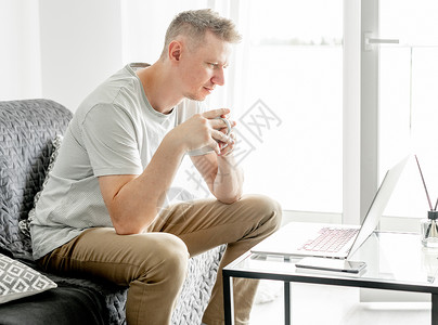 英俊的年轻人在笔记本电脑上工作工作者互联网办公客厅网络远程键盘白色沙发男人坐着高清图片素材