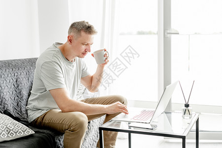 英俊的年轻人在笔记本电脑上工作成人男性工作者白色客厅商业自由职业者技术办公键盘网络高清图片素材