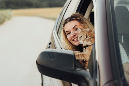 带着红猫从车窗向外看的白种年轻女子 同时享受周末公路之旅背景图片