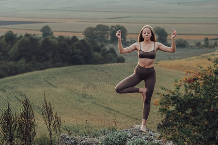 山顶瑜伽白种女青年在日落 山顶运动女孩进行冥想锻炼活动时带有全景景观的外门瑜伽练习成人岩石活力公园爬坡日出自由女性身体姿势背景