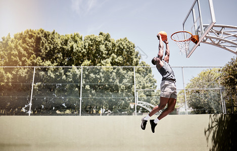 在球场上的比赛中 全长的篮球运动员将球扣入网中 适合和活跃的运动员在竞技比赛中跳跃得分 健康运动的非洲人在行动背景