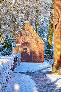 教堂冬天一个古老的教堂建筑的外部 有积雪的树木和小路 多雪的风景的小教堂与发光在砖墙上的太阳 冬季场景中欧式建筑的乡村背景
